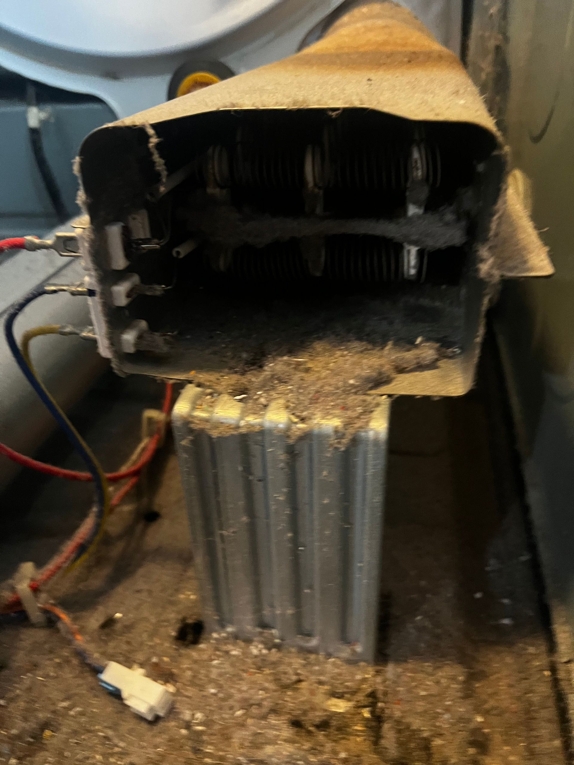 Burnt, damaged appliance with melted casing and exposed interior, sitting on a dusty floor.