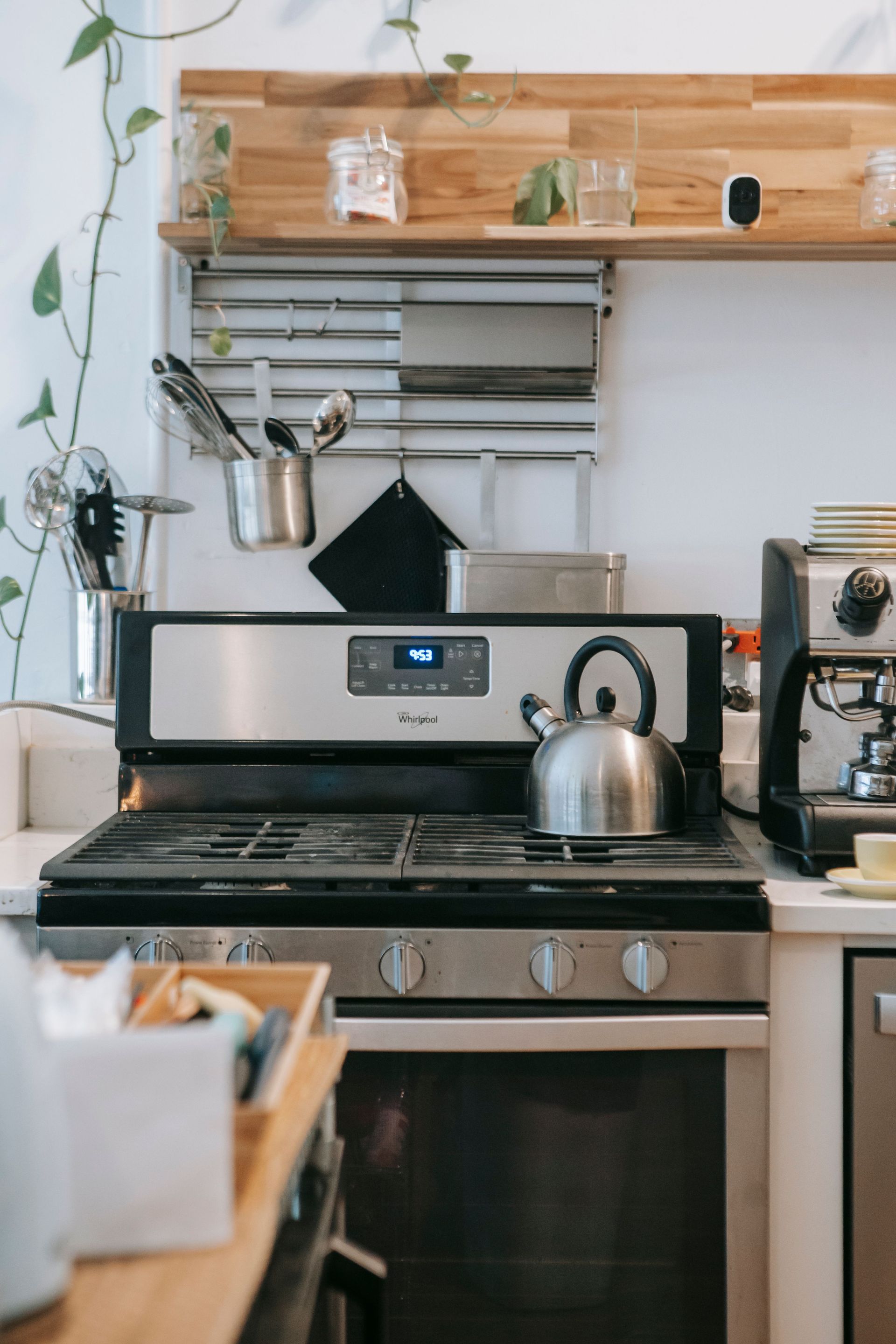 Modern kitchen stove with stainless steel kettle, hanging utensils, and wood shelf above it
