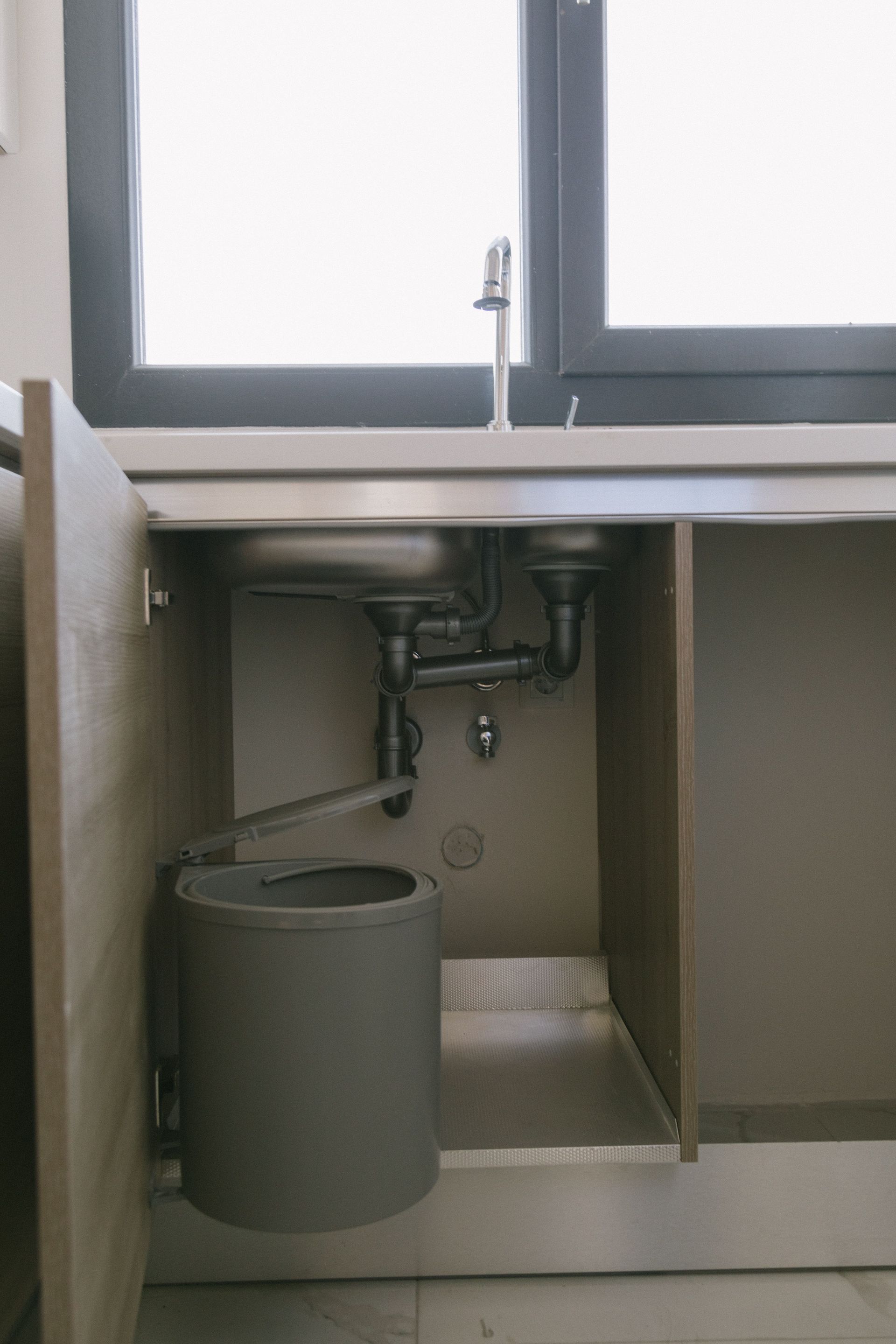 Small kitchen sink area with a gray trash bin under a window.