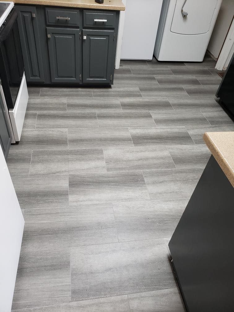 A view of gray wood-look vinyl plank flooring in a kitchen with gray cabinets and white appliances.