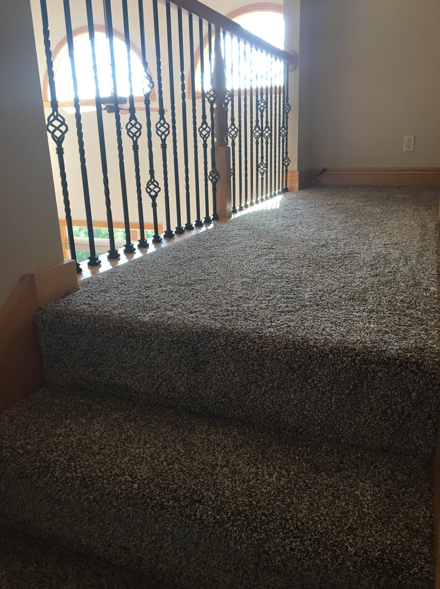 A staircase with dark speckled carpet and a black iron spindle railing against a beige wall.