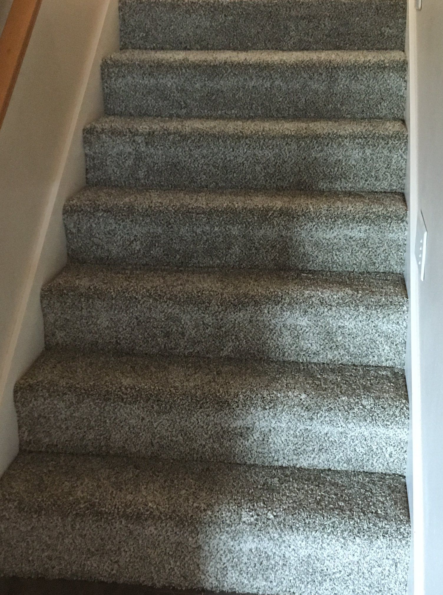 A set of stairs covered in speckled gray carpet, viewed from the bottom looking up between two walls.