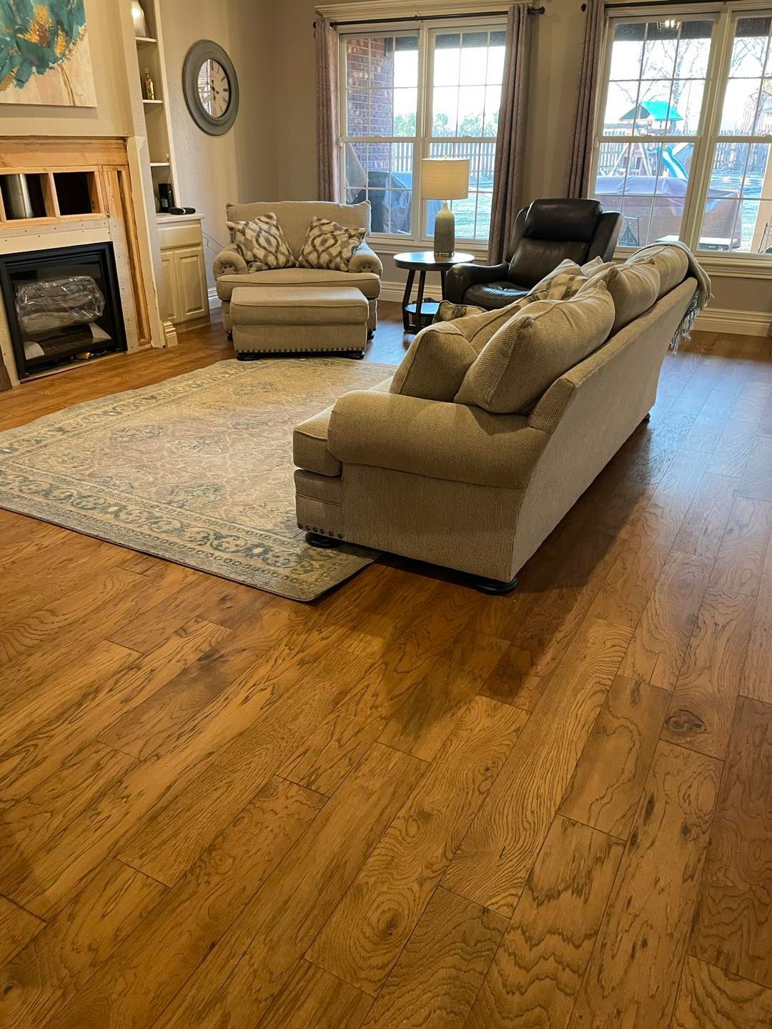 A living room with a beige sofa, matching armchair, fireplace, patterned rug, and wood floors.
