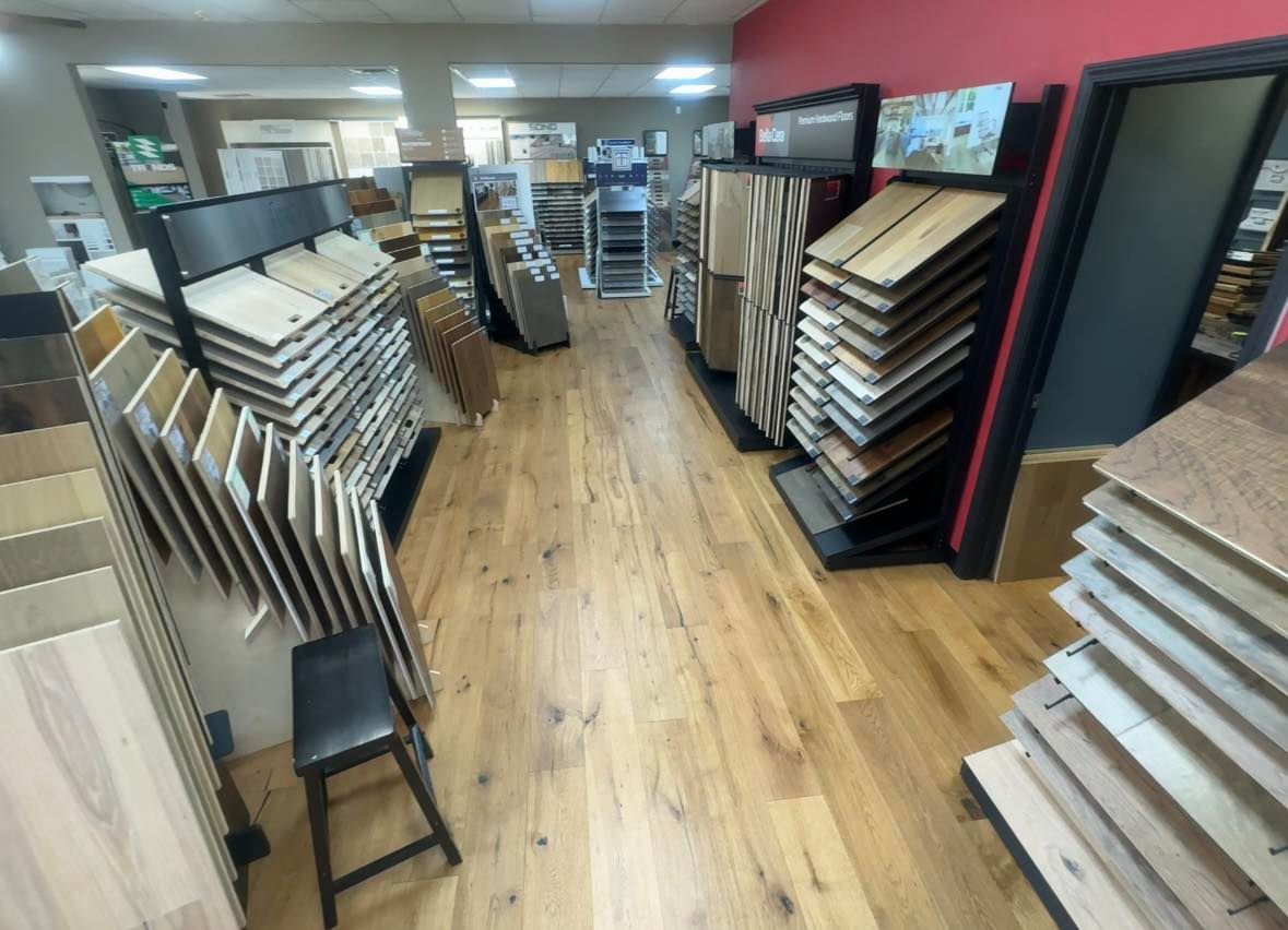 A showroom aisle displaying various wood and laminate flooring samples on standing racks, with hardwood flooring installed.