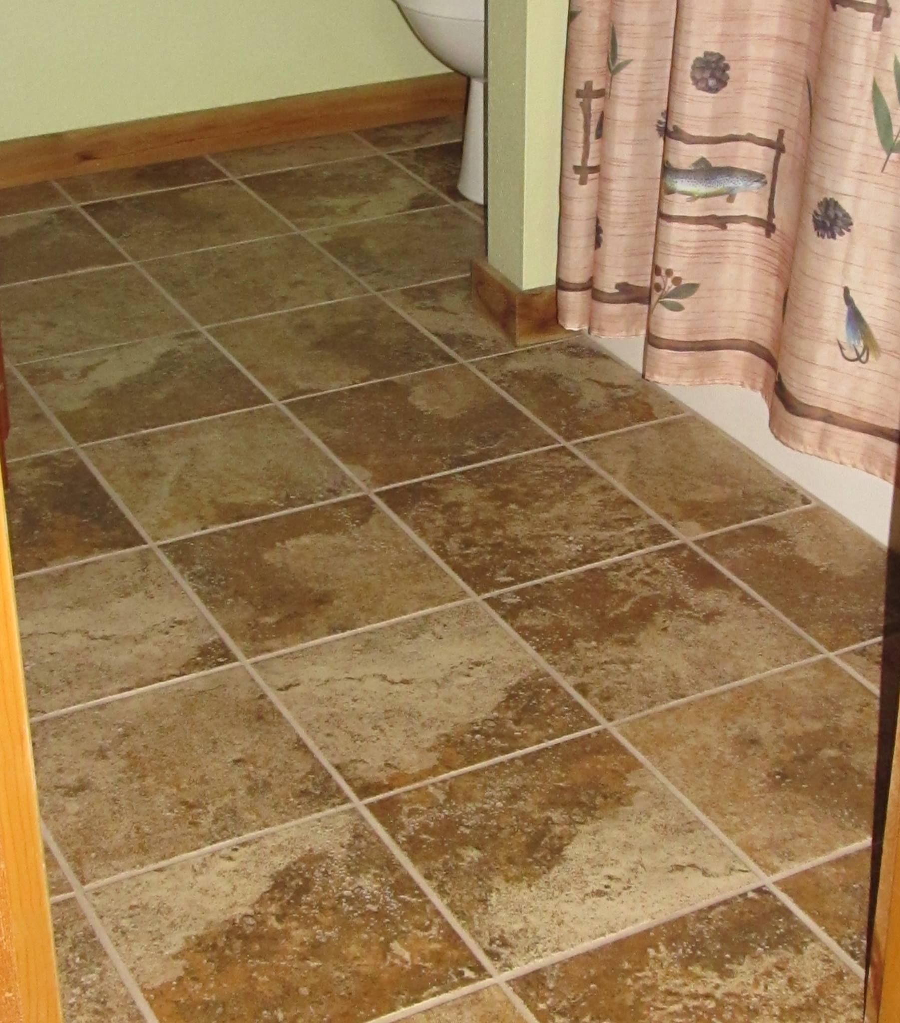 A bathroom floor with brown, mottled square tiles and a decorative shower curtain with fish and lure patterns.