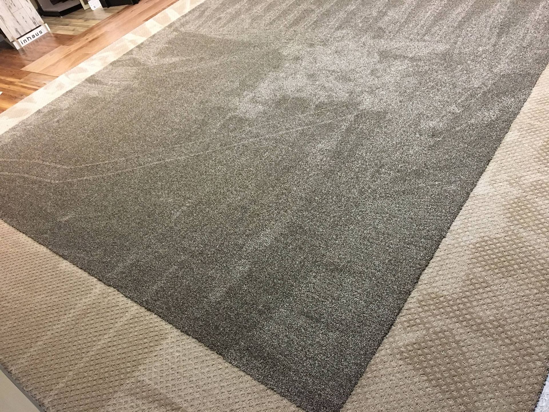 A rectangular gray carpet surrounded by a light beige carpet border on a wooden floor.