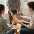 A professional showing wooden flooring samples to two people sitting in a living room.