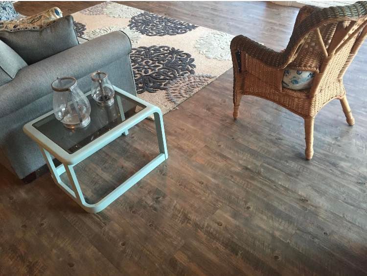 A cozy living area featuring a gray sofa, a light blue glass-topped side table with jars, a rattan chair, and a patterned rug.