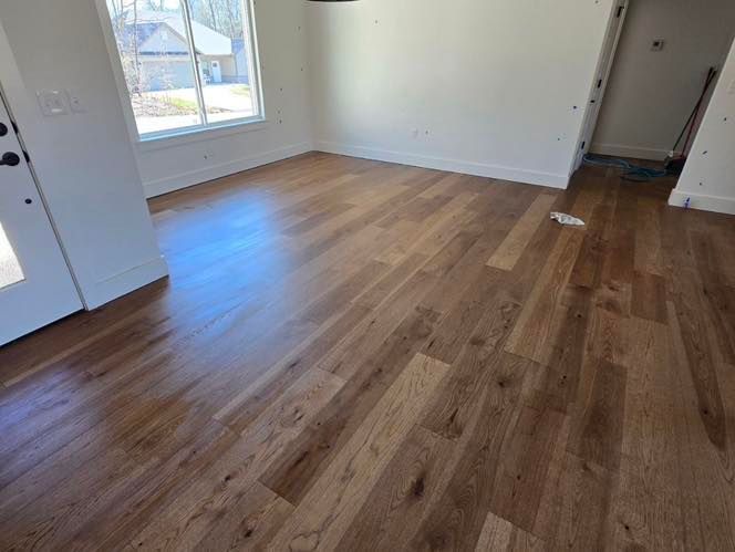 An interior room with light-colored walls and newly installed, wide-plank wood flooring with natural grain patterns.
