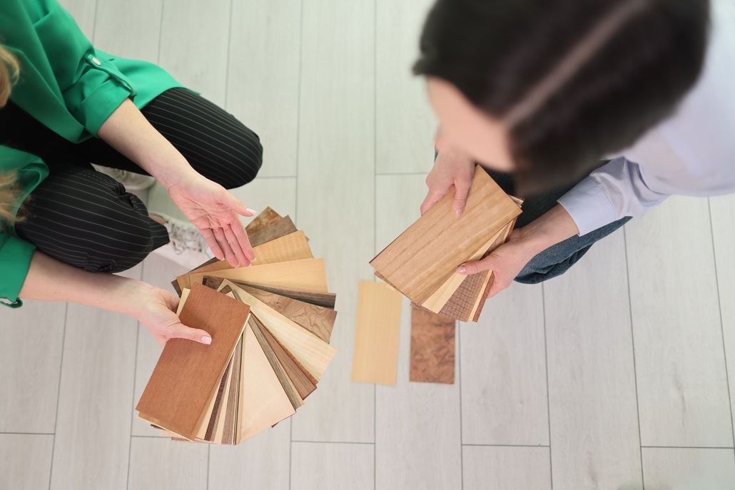 Two people comparing wood floor samples over a light wood floor Two people comparing wood floor samples over a light wood floor