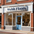 Storefront of Webb Floors with a blue door, large windows, and a brick exterior.