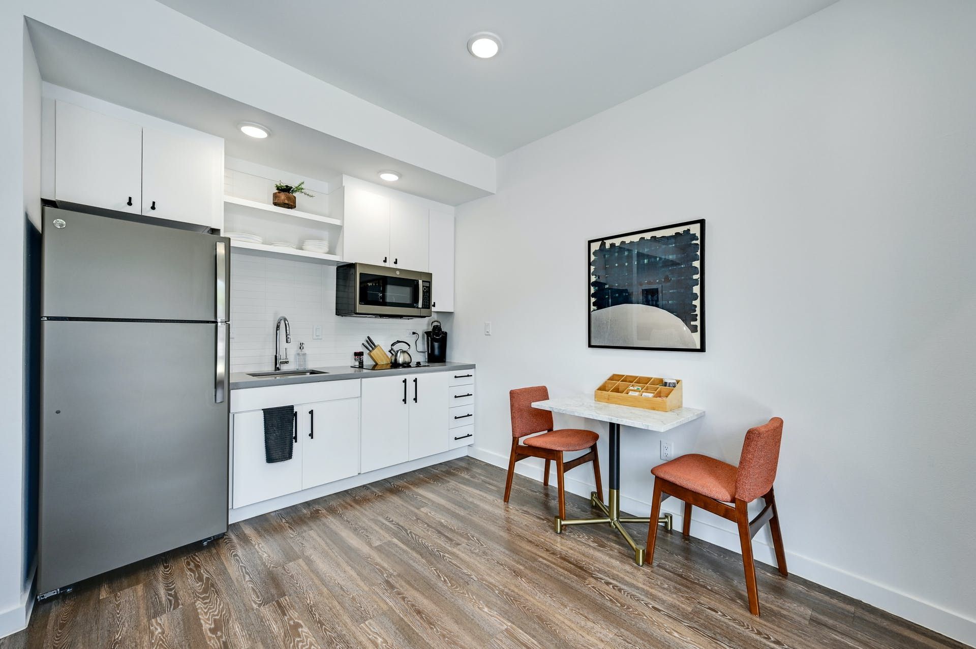 A kitchen with a refrigerator , microwave , sink , table and chairs.