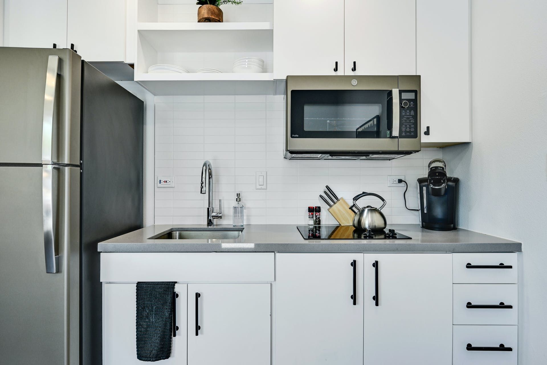 A kitchen with white cabinets , a stainless steel refrigerator , a microwave , and a sink.