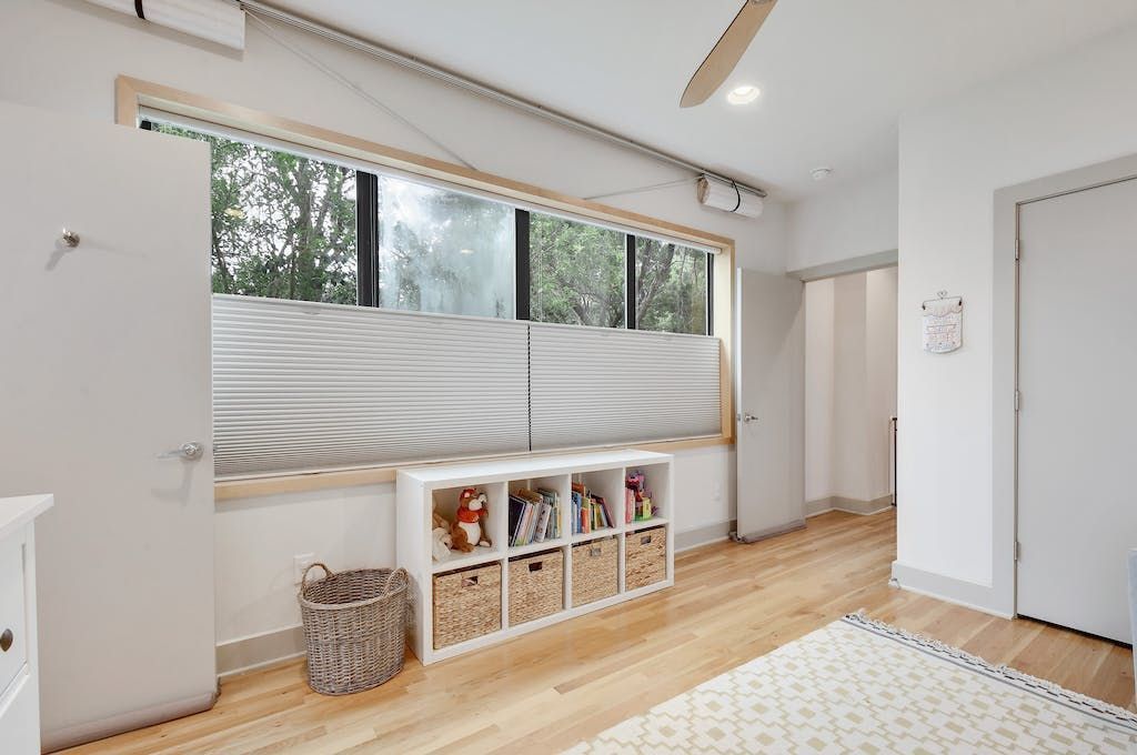 A bedroom with a large window , a shelf , and a ceiling fan.