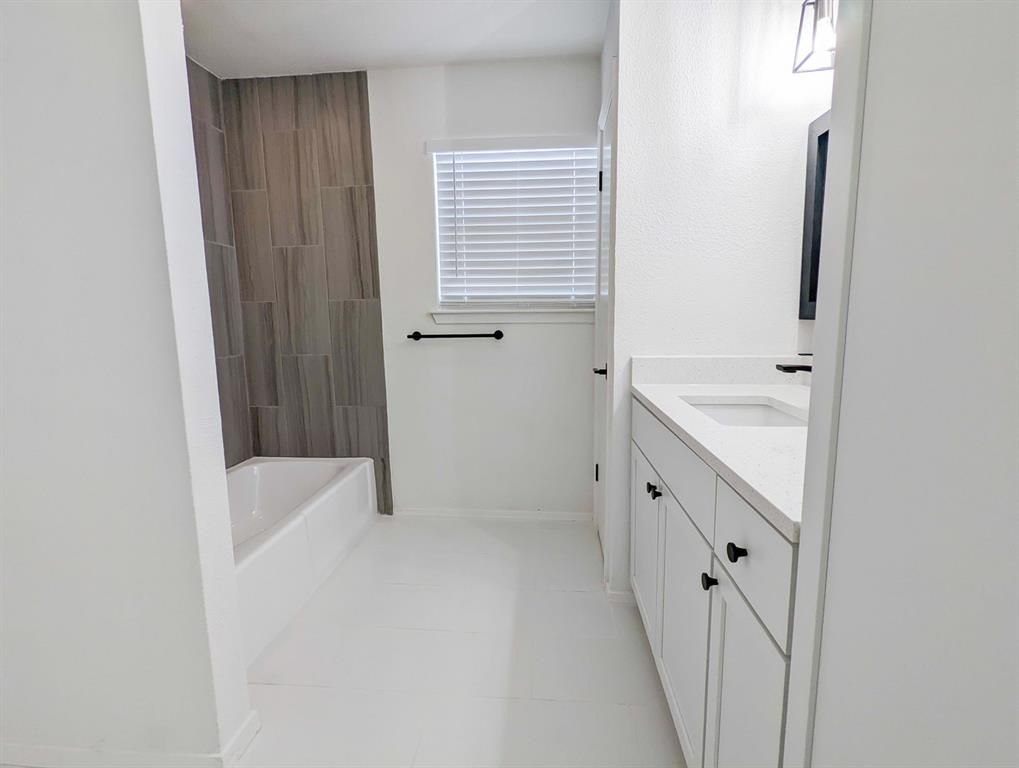 A bathroom with a tub , sink , mirror and window.