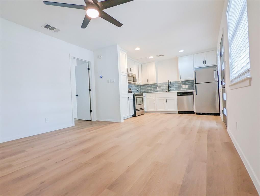 A living room with a ceiling fan and a kitchen with stainless steel appliances.