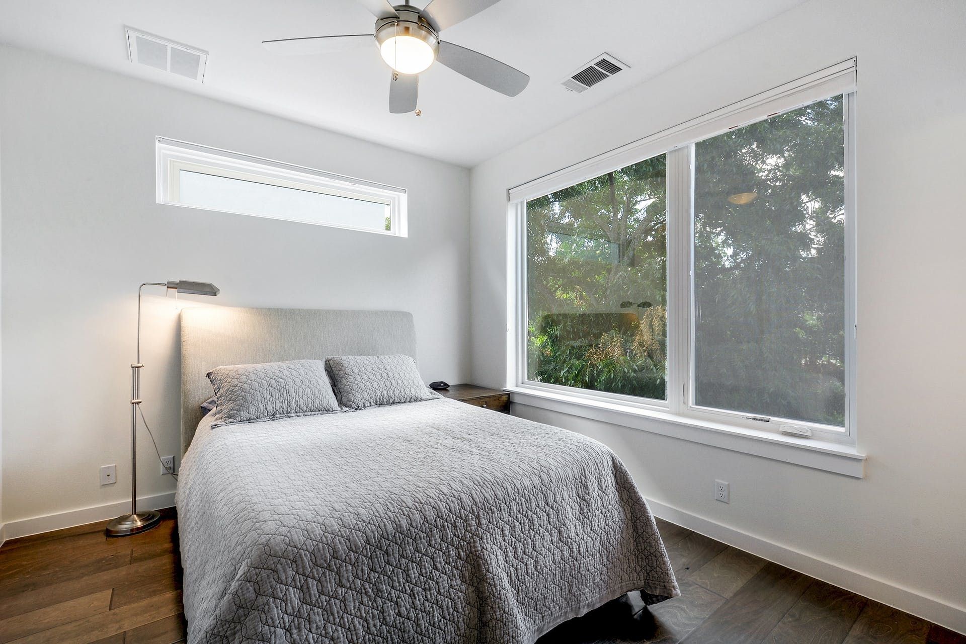 A bedroom with a bed , ceiling fan , and large windows.