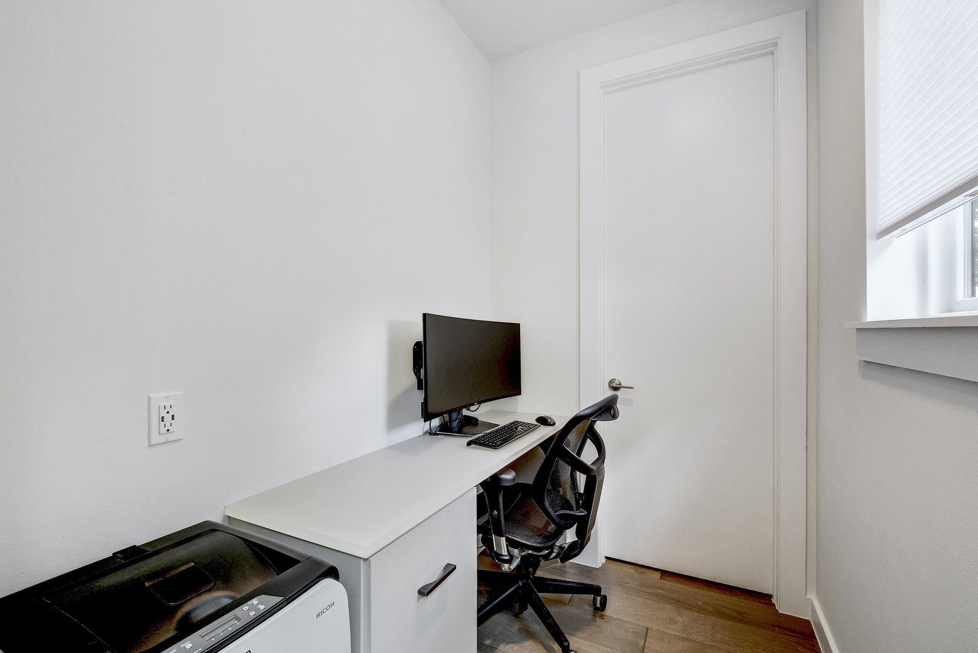 A small office with a desk , chair , computer and printer.