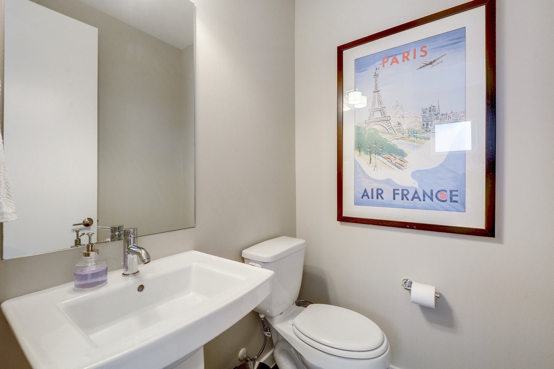 A bathroom with a sink , toilet and a picture of paris on the wall.
