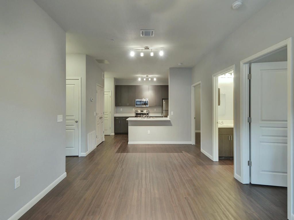A living room with hardwood floors and a kitchen in the background.