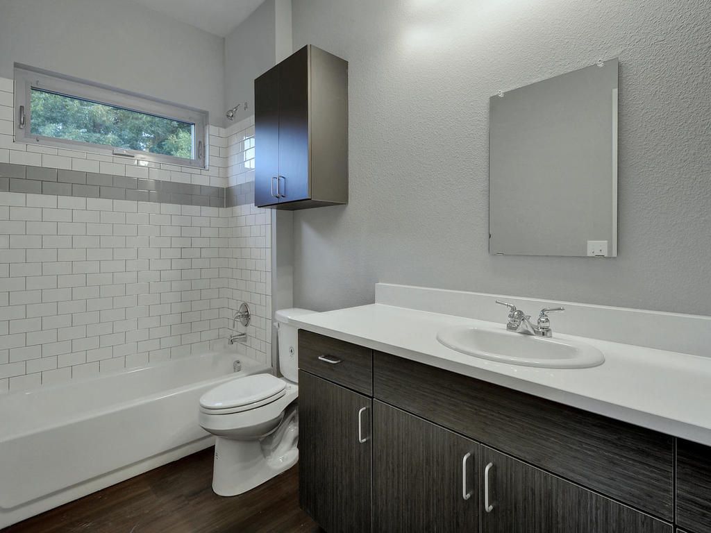 A bathroom with a toilet , sink , tub and mirror.