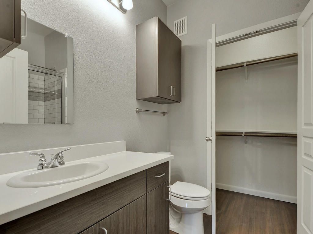 A bathroom with a sink , toilet , mirror and walk in closet.