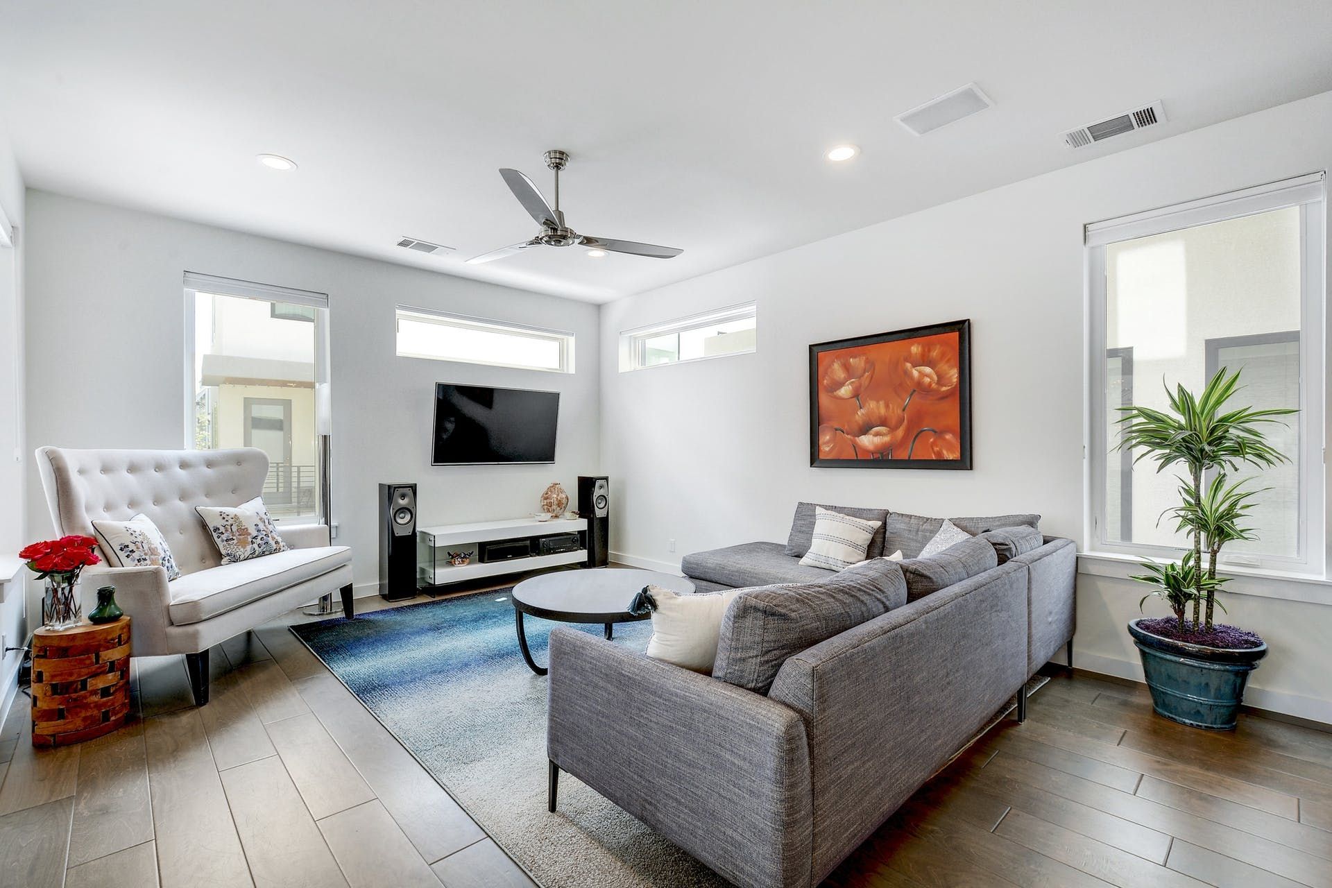 A living room with a couch , chairs , a television and a ceiling fan.