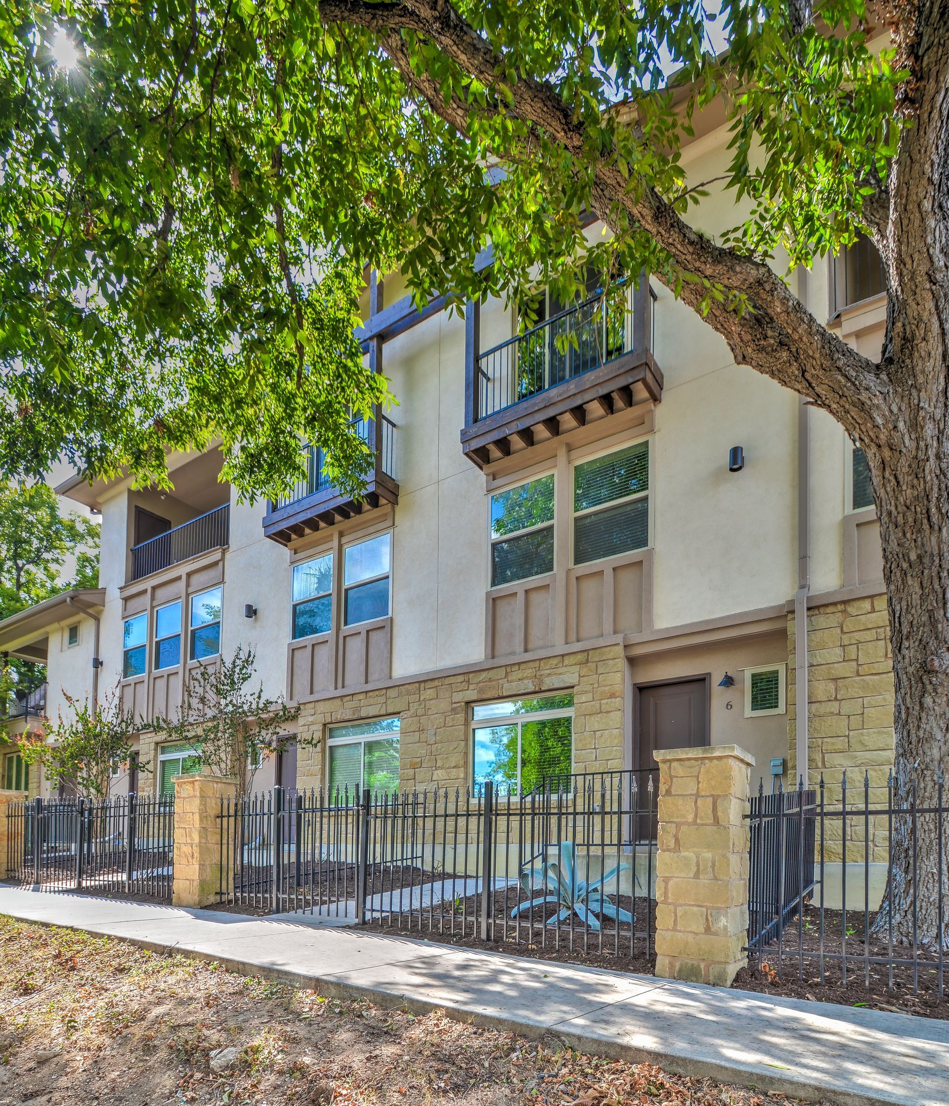 A large apartment building with a fence and a tree in front of it.