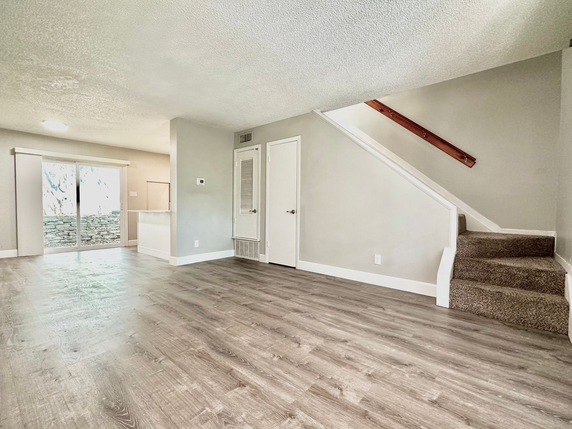 An empty living room with hardwood floors and stairs leading up to the second floor.