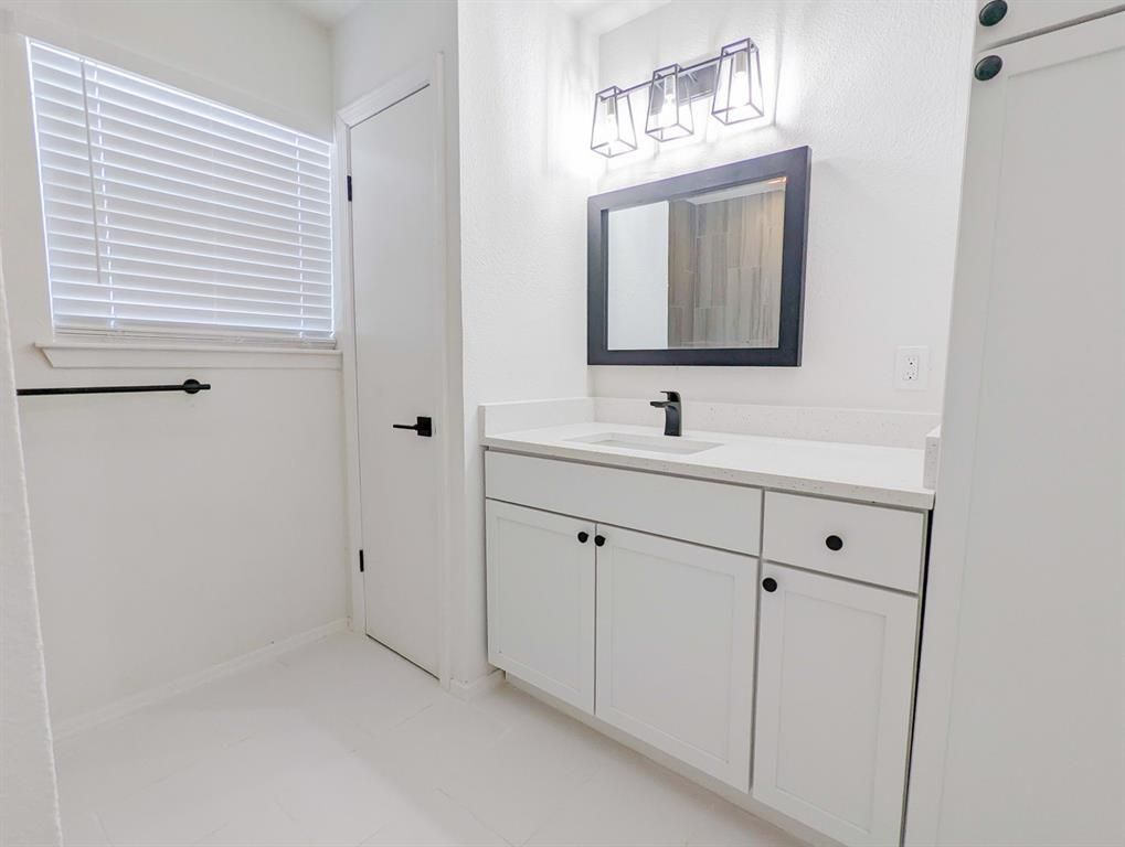 A bathroom with white cabinets , a sink , a mirror and a window.