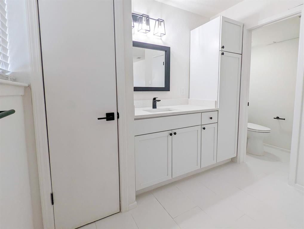 A bathroom with white cabinets , a sink , a mirror and a toilet.