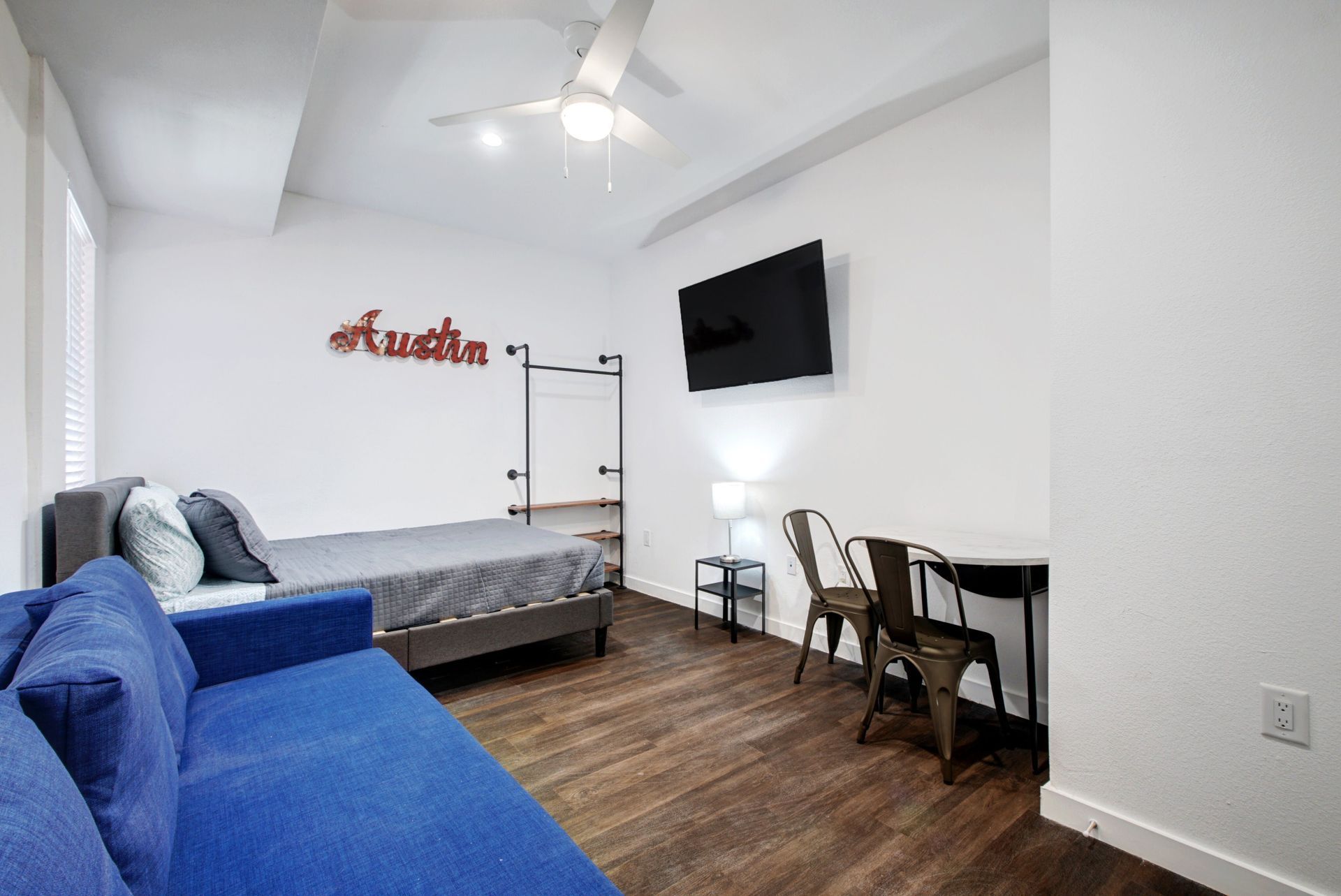 A bedroom with a blue couch , a bed , a table and chairs.