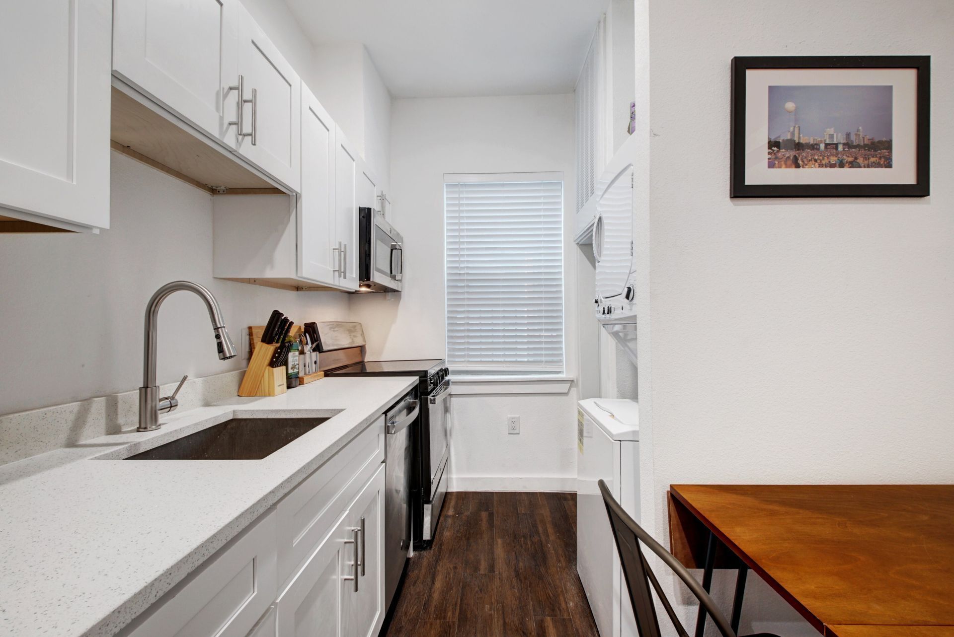 A kitchen with white cabinets , stainless steel appliances , a sink and a table.