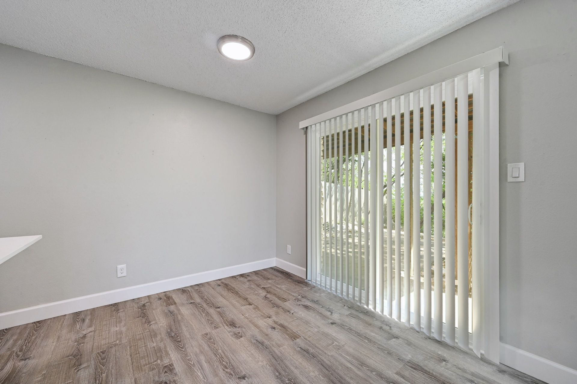 An empty room with a sliding glass door and blinds.