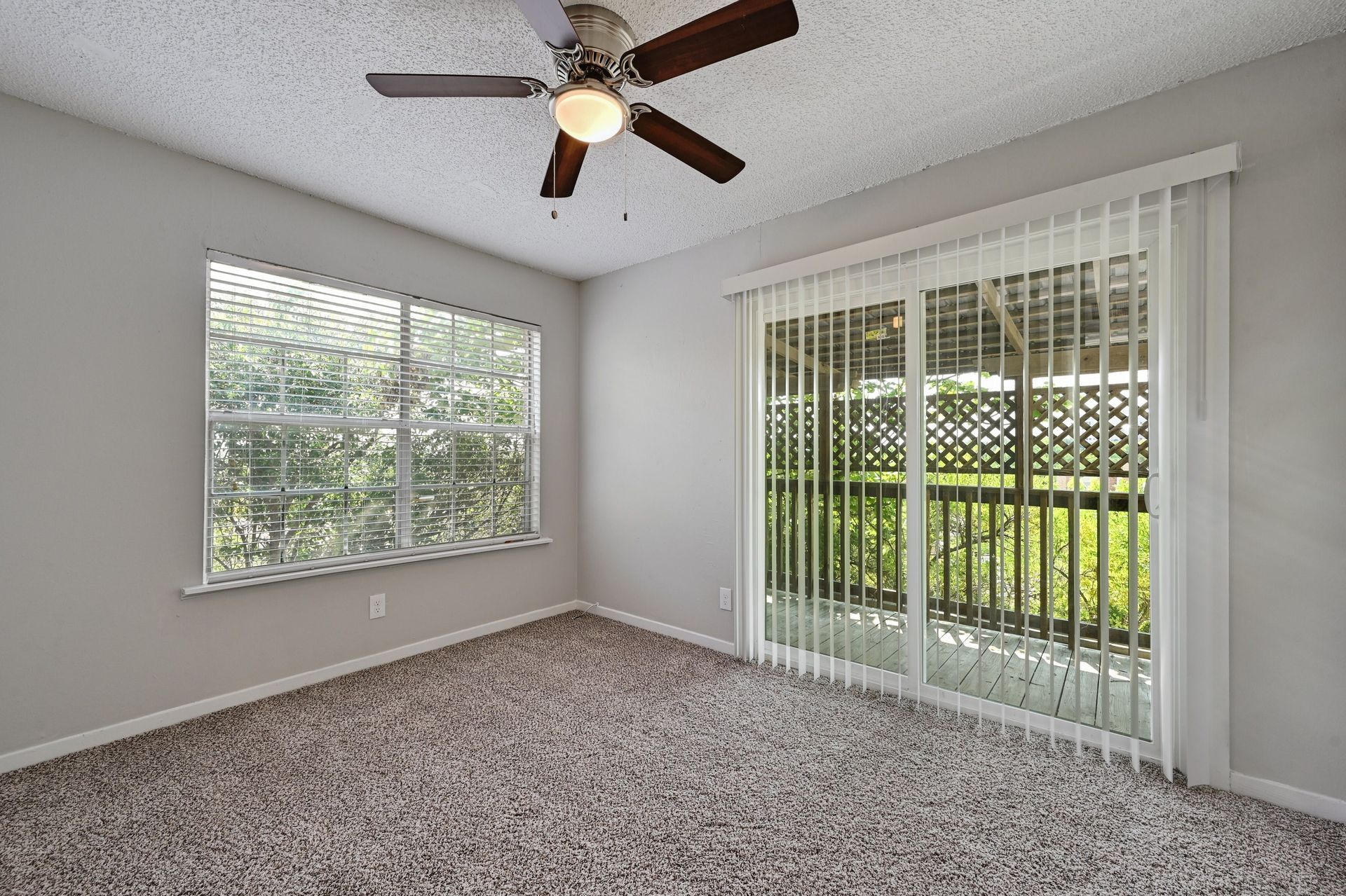 An empty living room with a ceiling fan and sliding glass doors.