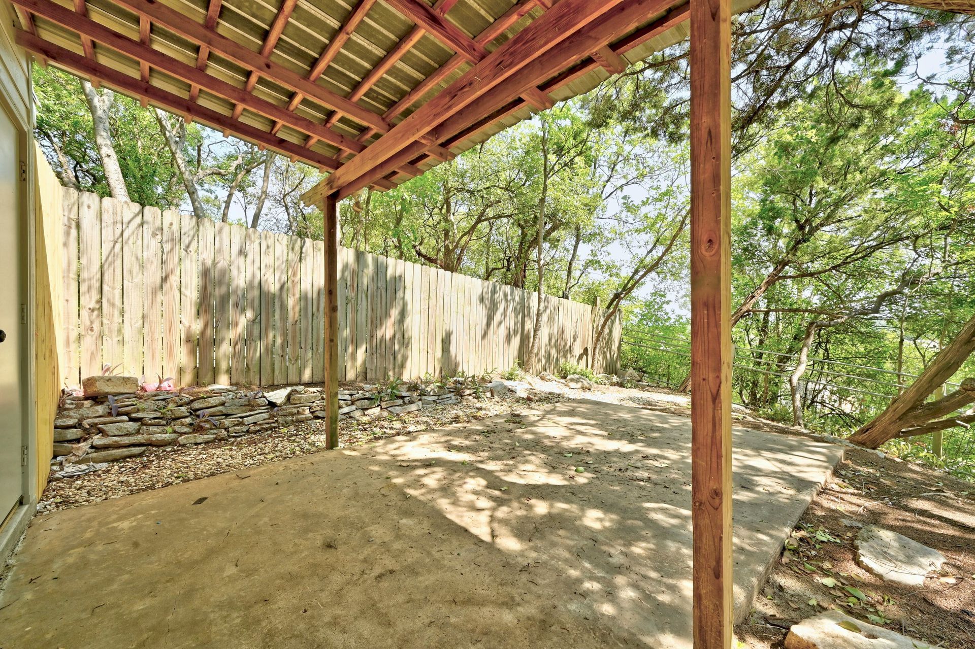 A covered patio with a wooden fence and trees in the background.