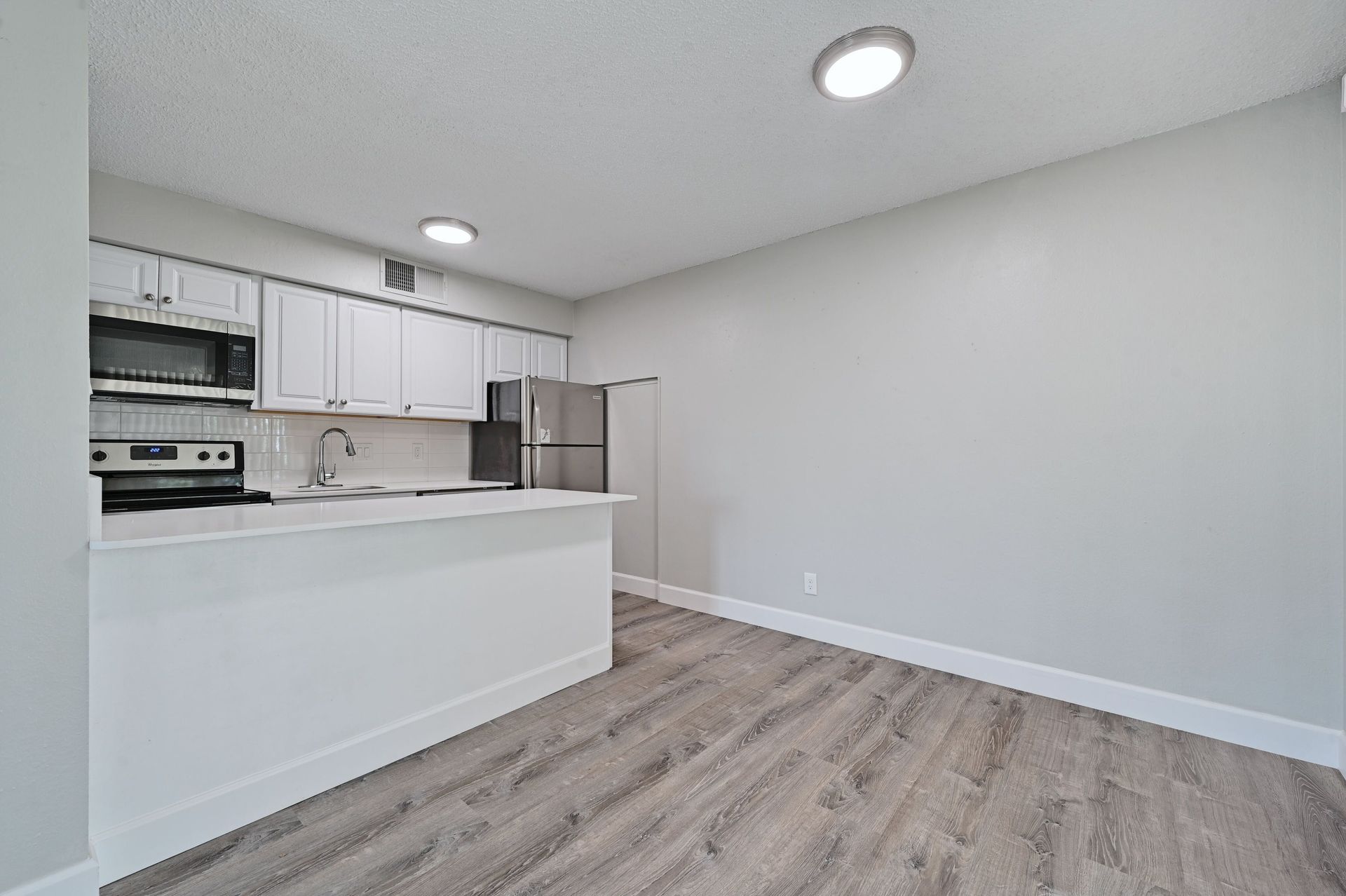 A kitchen with white cabinets , stainless steel appliances , a refrigerator and a microwave.
