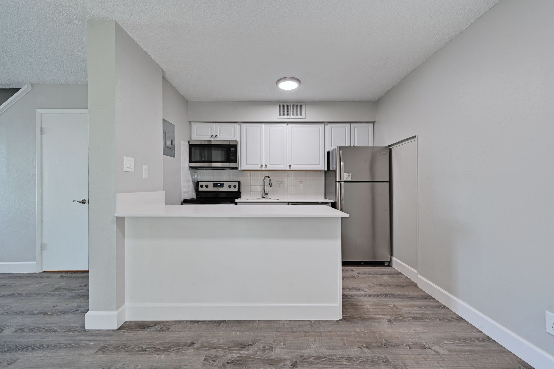 A kitchen with white cabinets , stainless steel appliances , a refrigerator and a microwave.