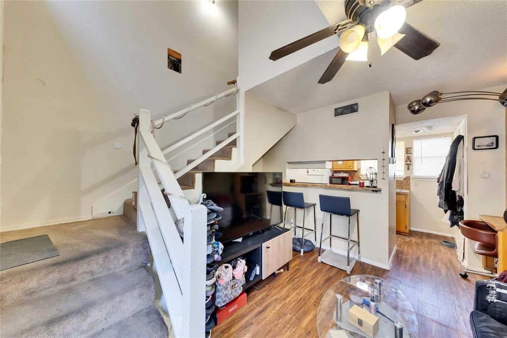 A living room with stairs leading up to the second floor and a ceiling fan.