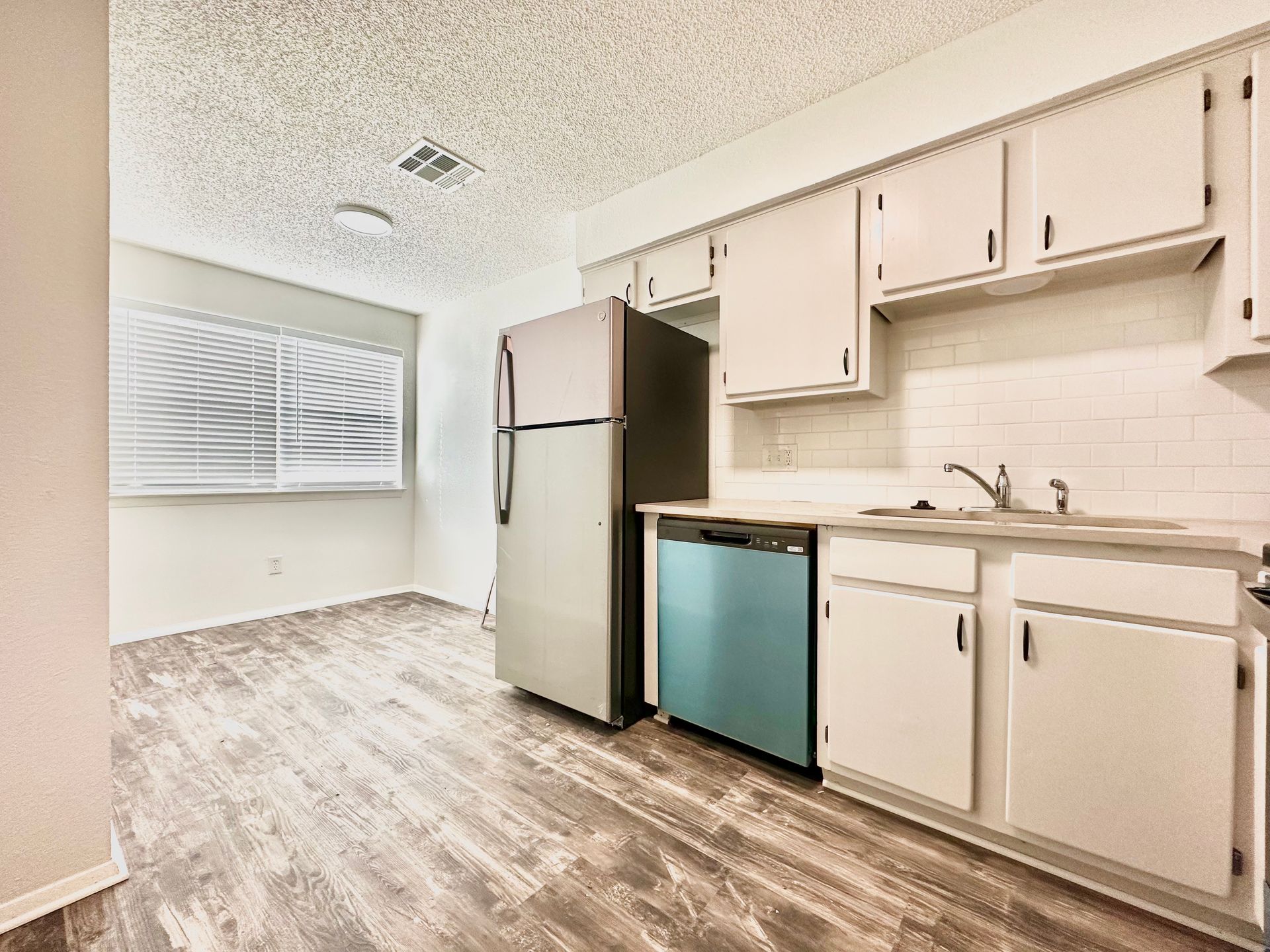A kitchen with white cabinets , a refrigerator , a sink , and a blue dishwasher.