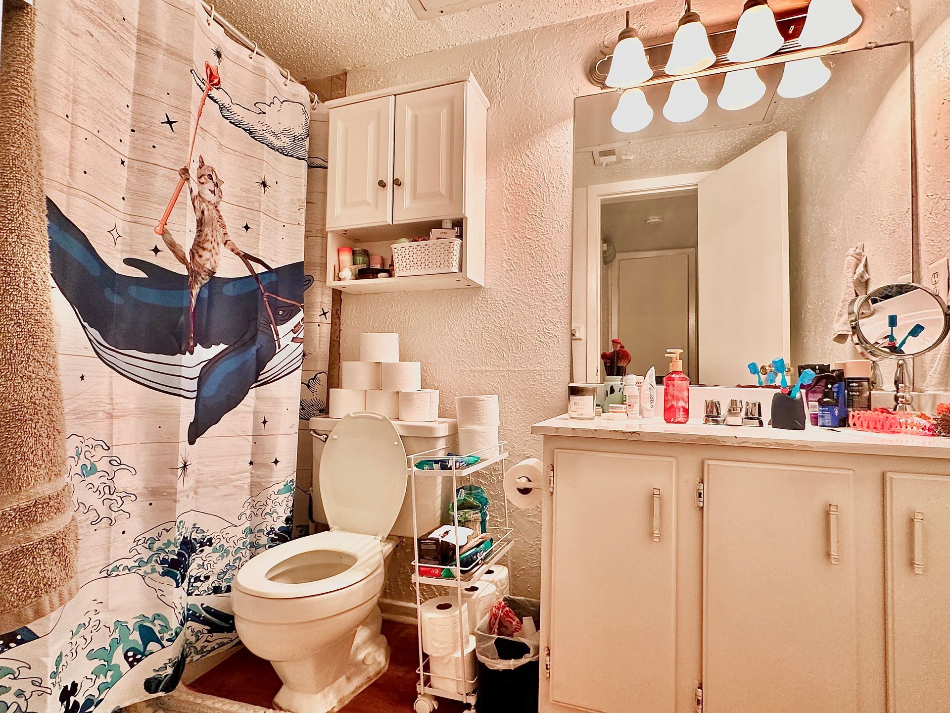 A bathroom with a toilet , sink , mirror and shower curtain with a whale on it.