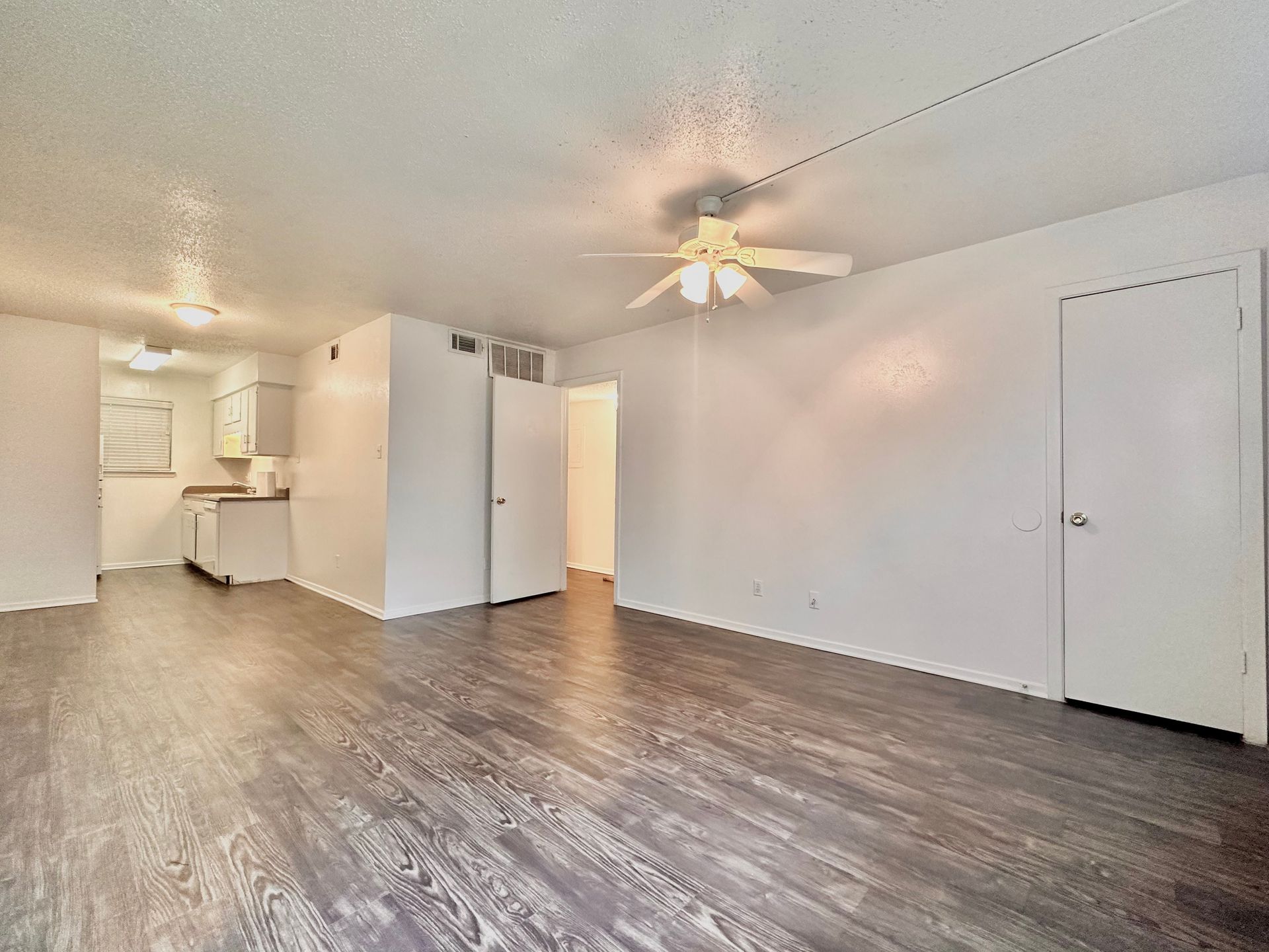 An empty living room with hardwood floors and a ceiling fan.