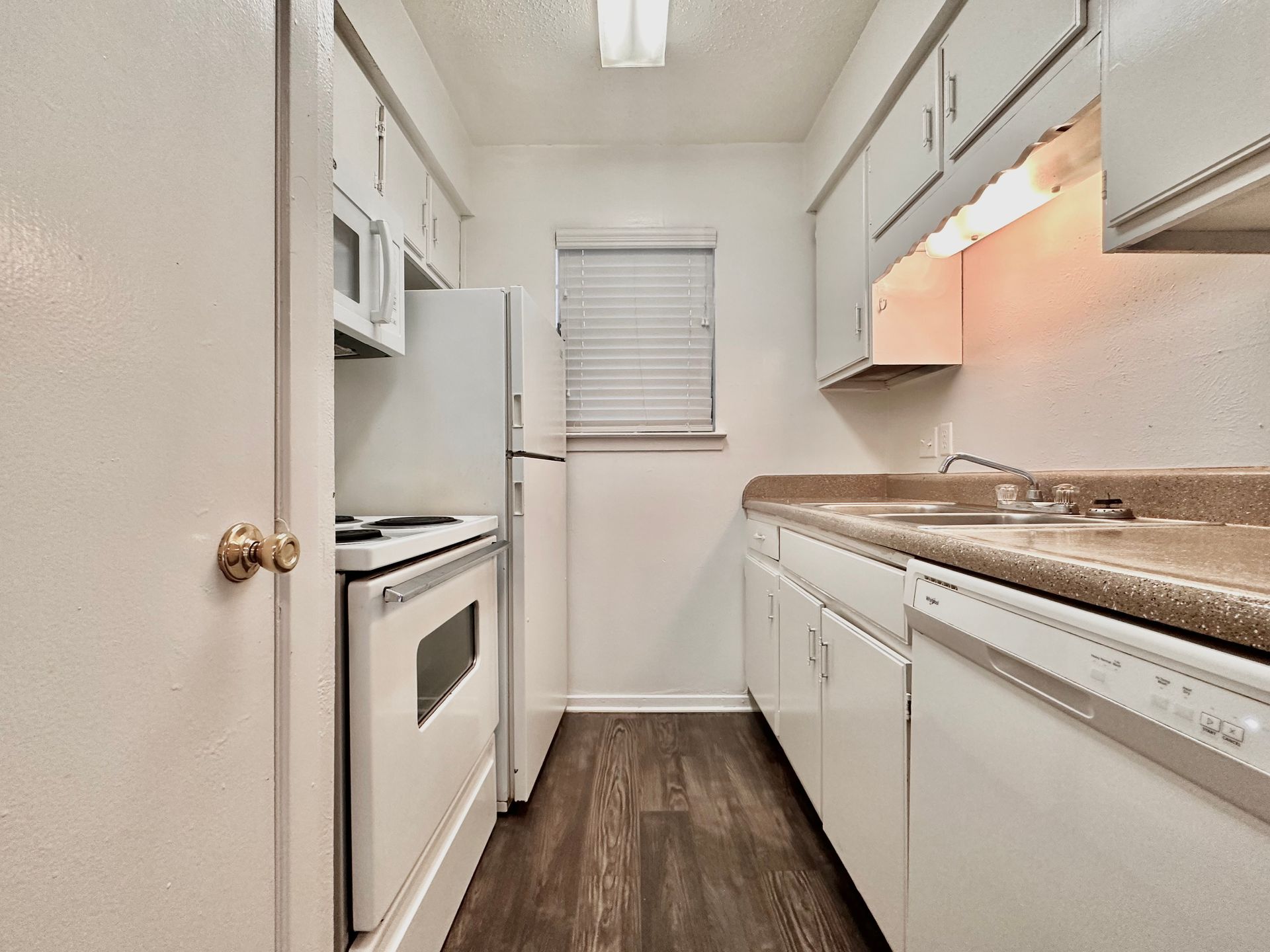 A kitchen with white cabinets , a refrigerator , a stove , a sink , and a window.