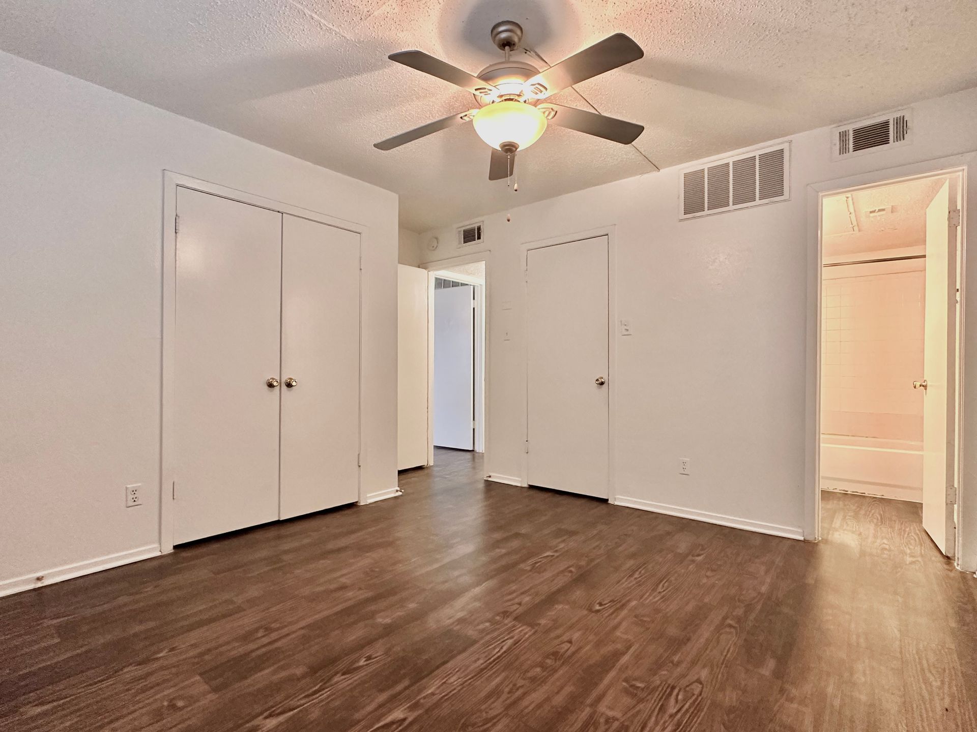 An empty bedroom with hardwood floors and a ceiling fan.