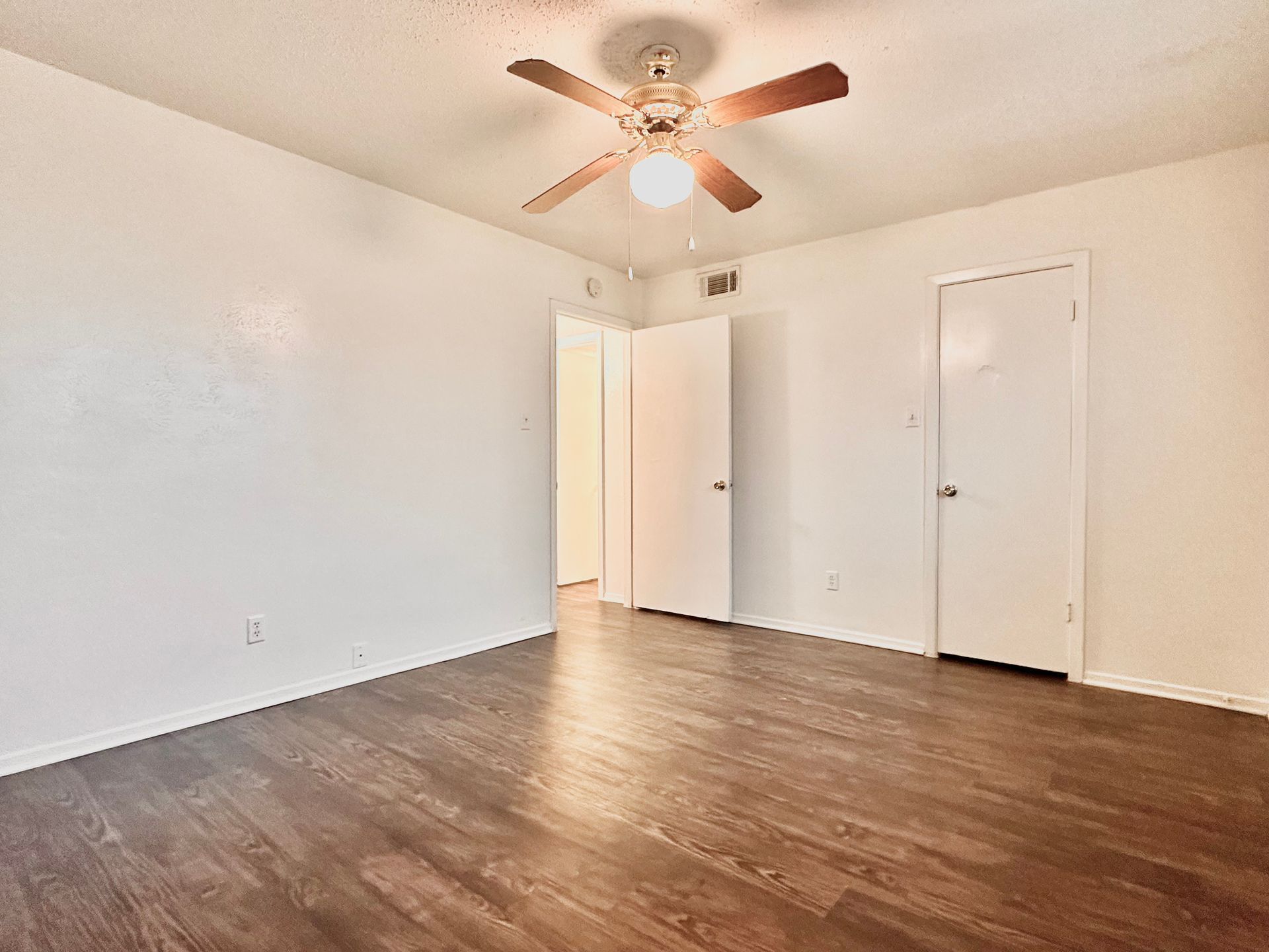An empty bedroom with hardwood floors and a ceiling fan.