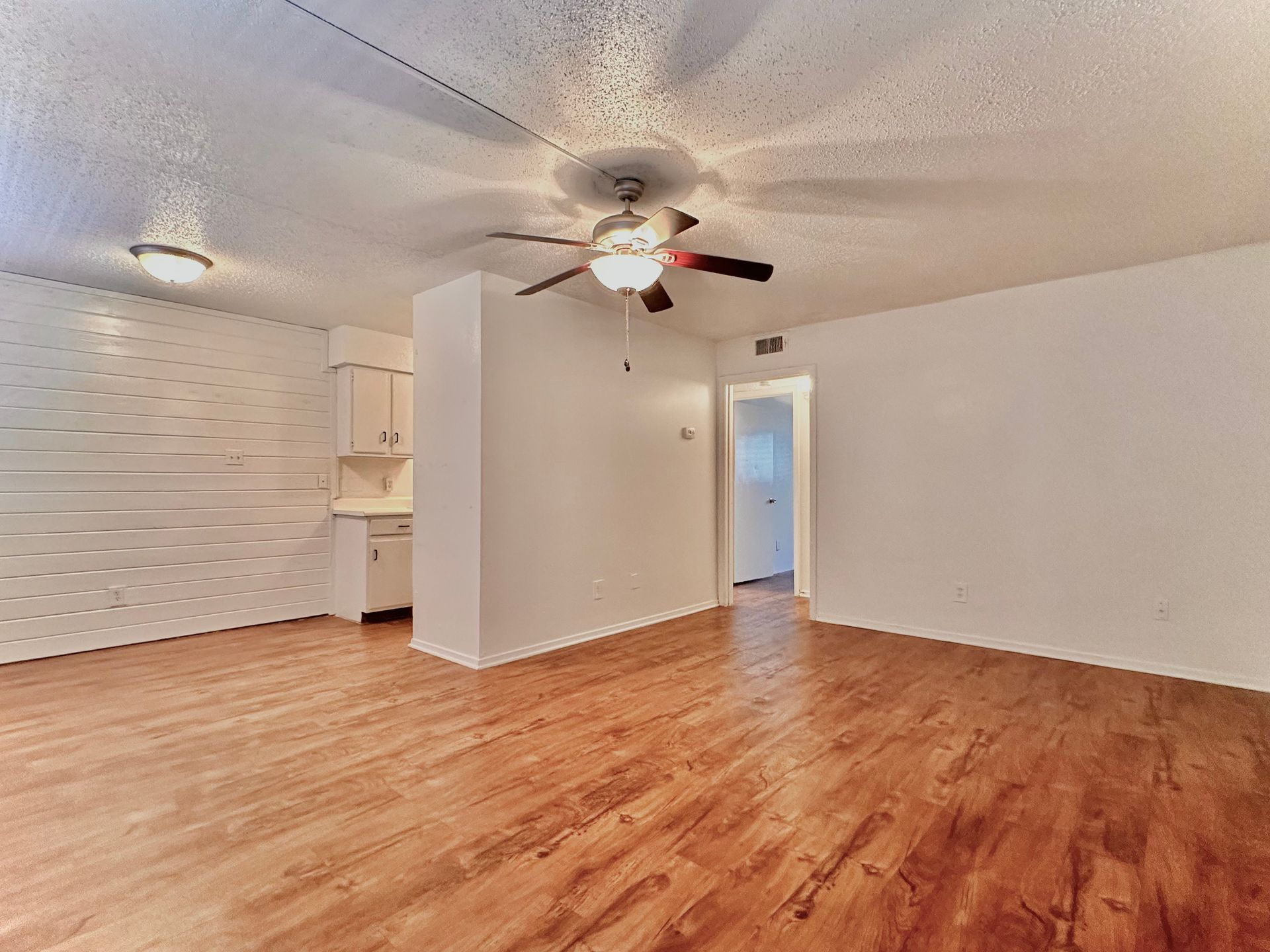 An empty living room with hardwood floors and a ceiling fan.