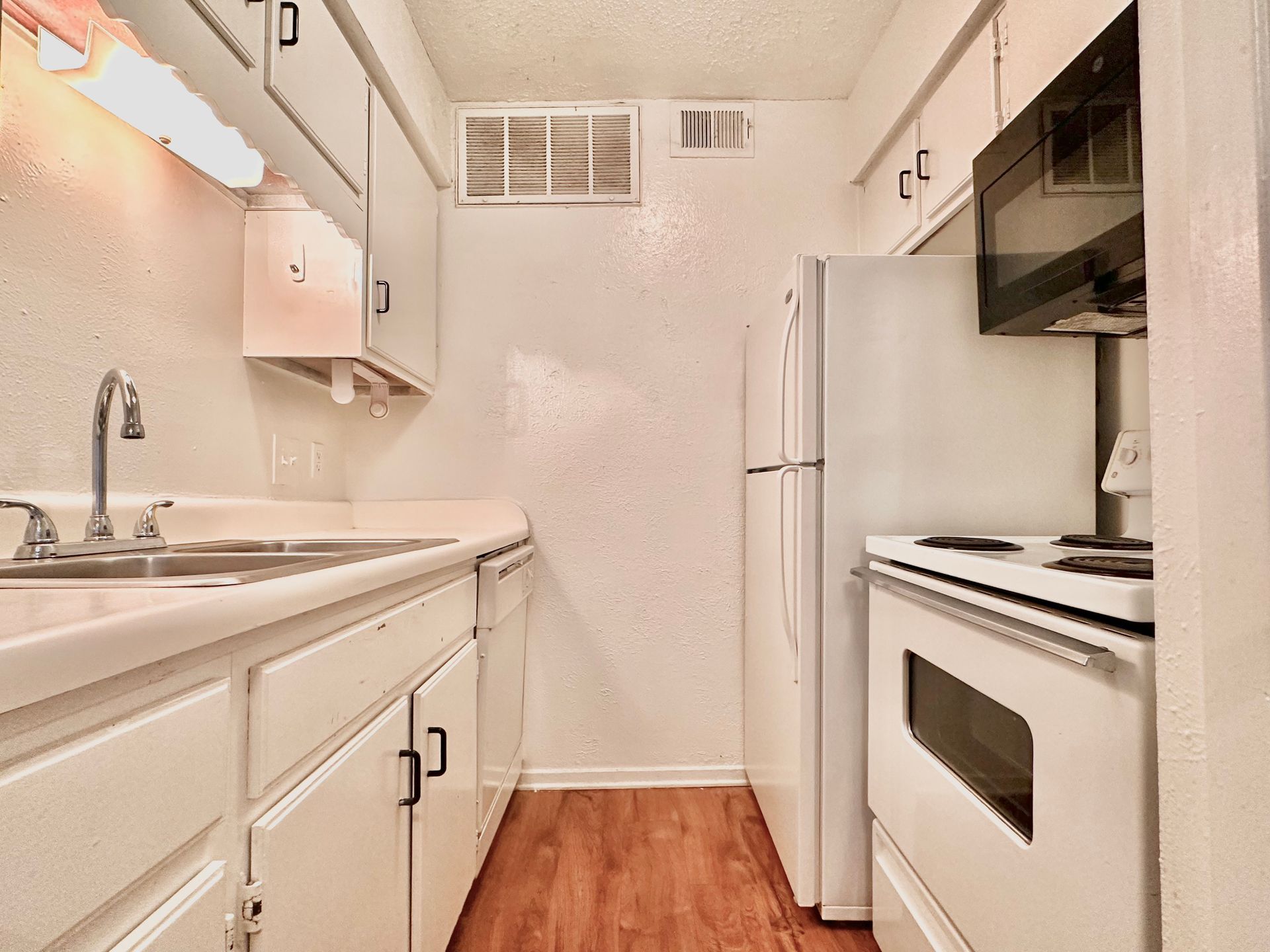 A kitchen with white cabinets , a refrigerator , stove and microwave.