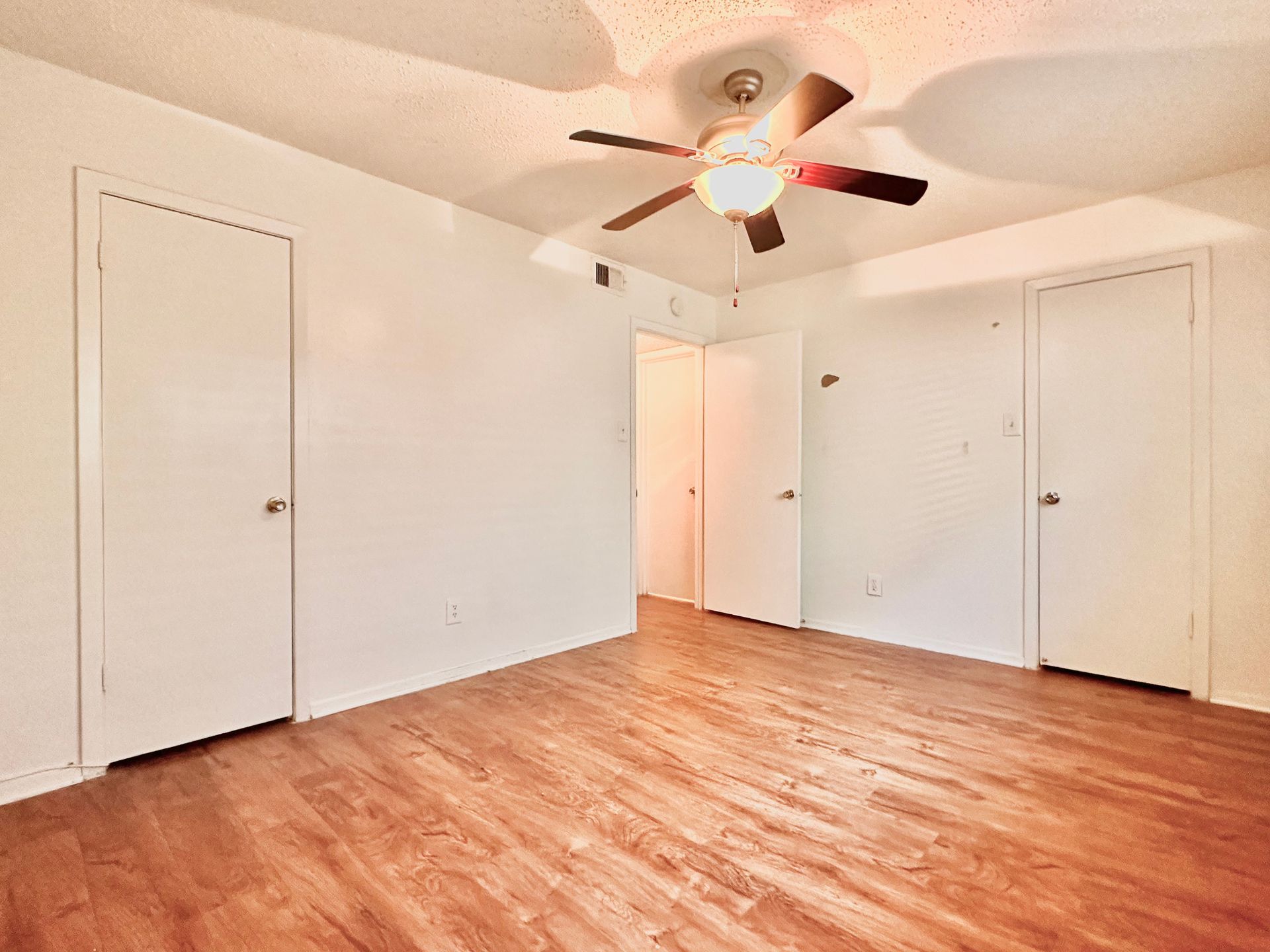 An empty bedroom with hardwood floors and a ceiling fan.