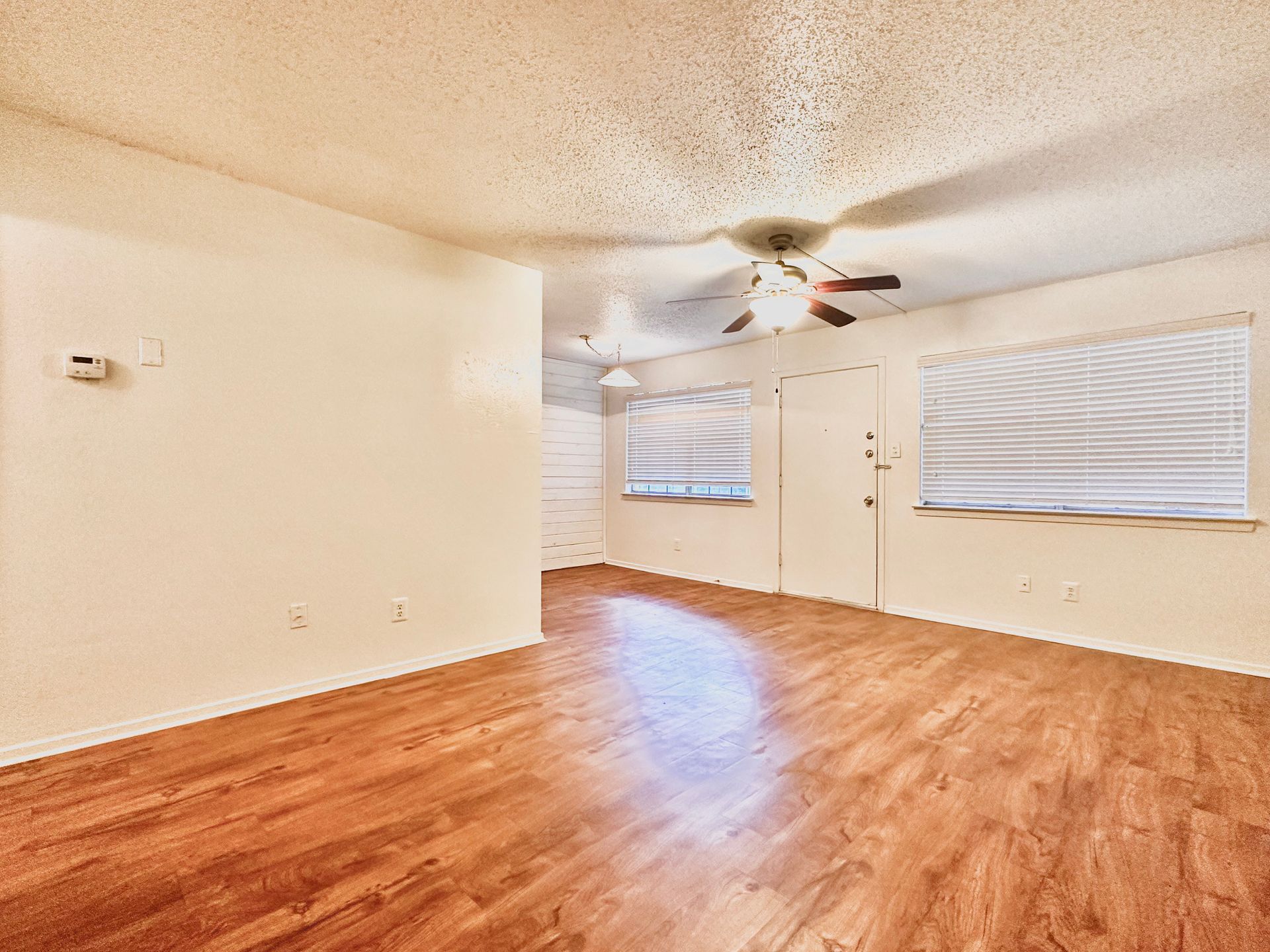 An empty living room with hardwood floors and a ceiling fan.