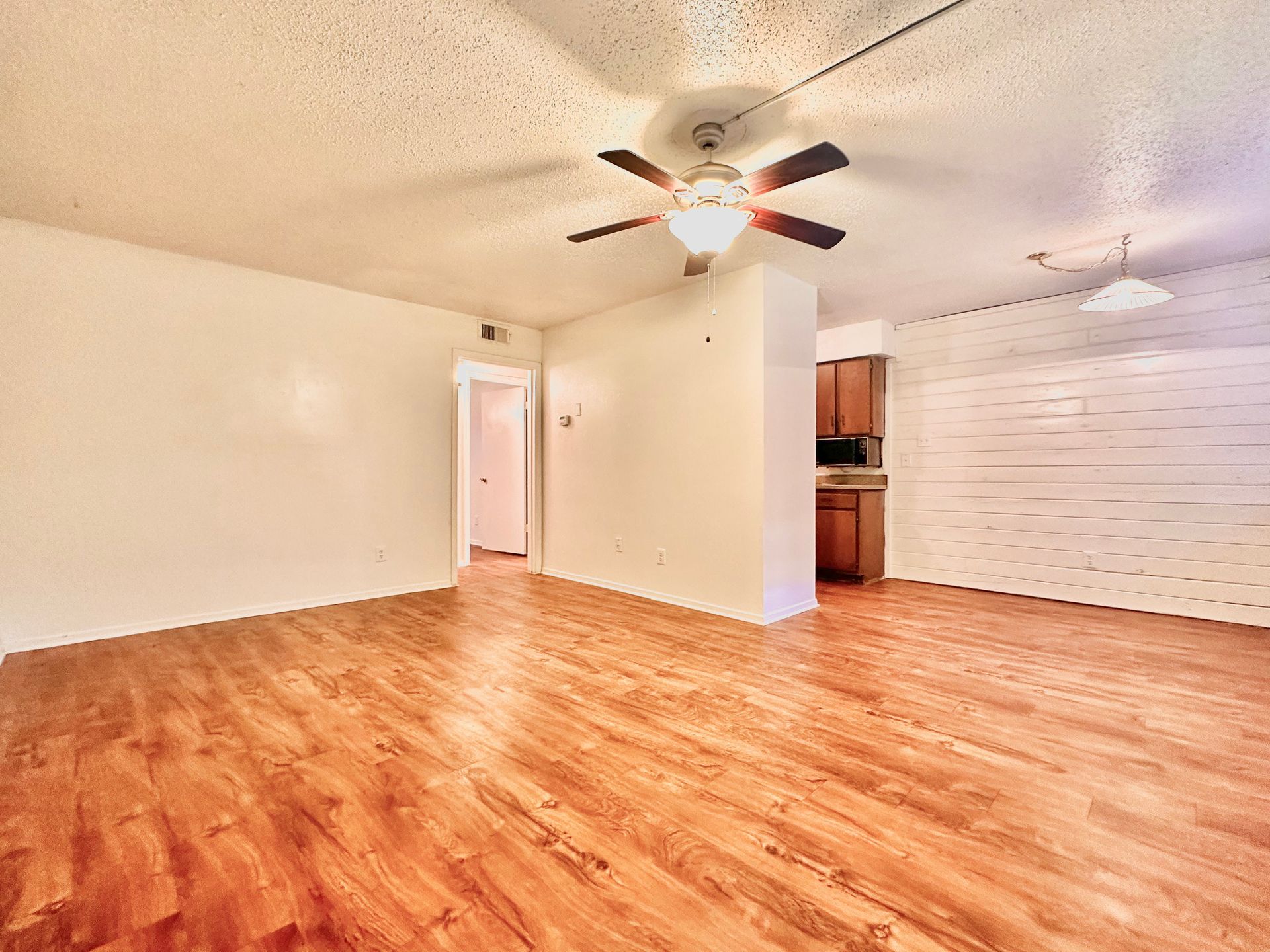 An empty living room with hardwood floors and a ceiling fan